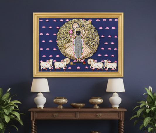 Hand-painted Pichwai painting of Shrinathji with cows and lotus motifs in a gold frame on wall.