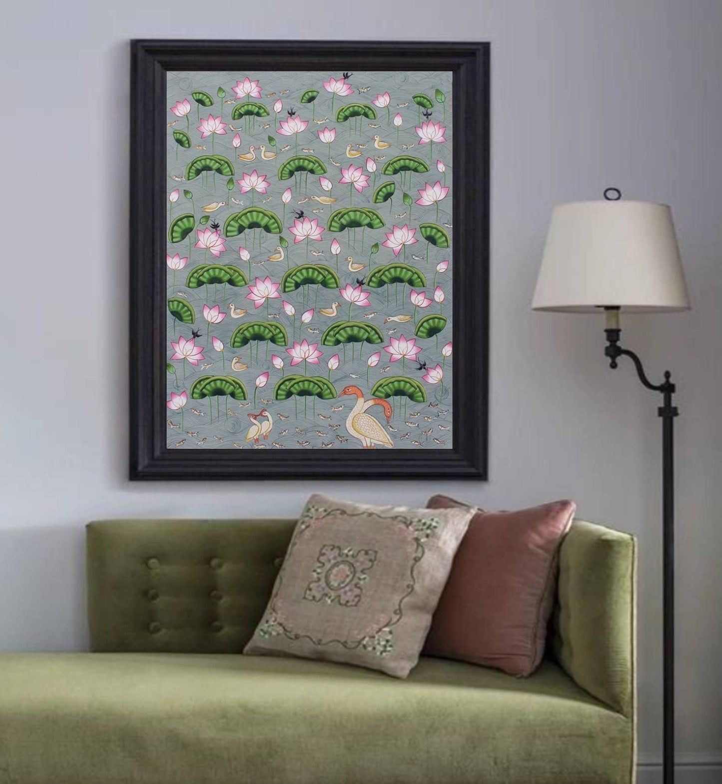 Framed Pichwai painting with lotus flowers, birds, and lily pads on a wall above a green sofa.